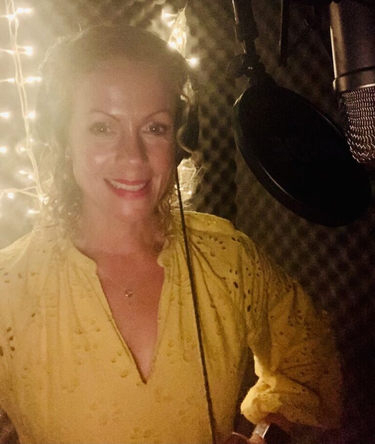 Yellow Dress smiling in voice over studio with Rode mic, pop filter, cords and sound treatment